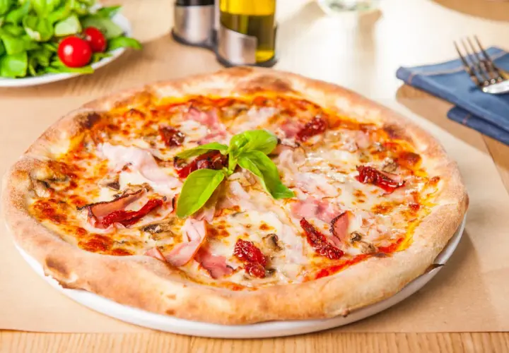 Une délicieuse pâte à pizza garnie de jambon, de tomates séchées et de basilic frais, prête à être dégustée.