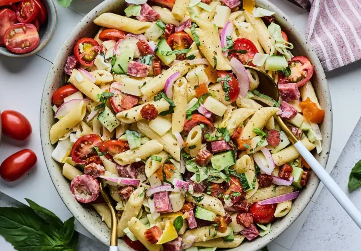 Salade de pâtes généreuse avec penne, tomates cerises, concombre, salami et oignons rouges. Un plat frais et coloré.