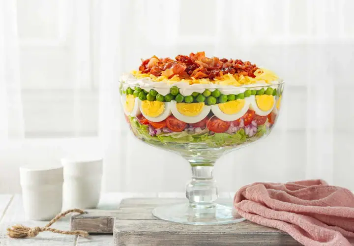 Une magnifique salade 7 étages, présentée dans un grand bol en verre, avec des couches de légumes frais, d'œufs durs, de petits pois et de bacon croustillant sur le dessus.