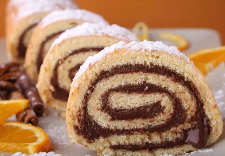 Tranches de roulé au chocolat saupoudrées de sucre glace, accompagnées d'oranges et de bâtons de cannelle.