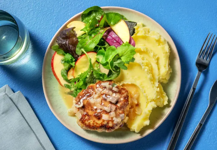 Un steak haché sauce oignons, servi avec une généreuse portion de purée de pomme de terre et une salade croquante aux pommes.