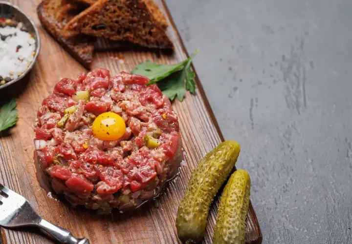Un délicieux tartare de boeuf, garni d'un jaune d'œuf, servi avec des cornichons, du pain grillé et des épices.