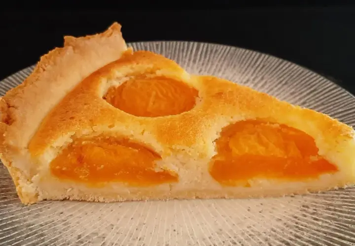 Tranche de tarte aux abricots classique, avec sa pâte dorée et ses fruits juteux, prête à être dégustée.