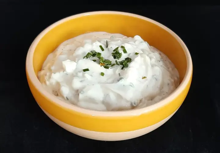 Sauce onctueuse à base de fromage blanc et de ciboulette fraîche, garnie de brins d'herbe verte.