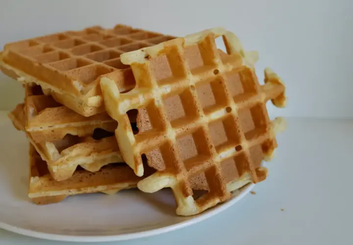 Pile de gaufres dorées sur une assiette blanche. La pâte à gaufre a été cuite à la perfection, offrant une texture croustillante et moelleuse.