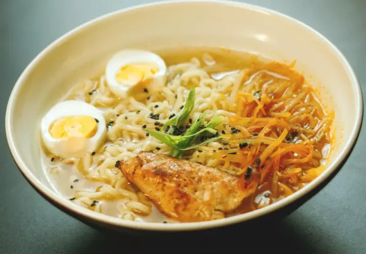 Un bol de recette ramen poulet, garni d'œufs durs, de poulet grillé, de nouilles et de ciboule.