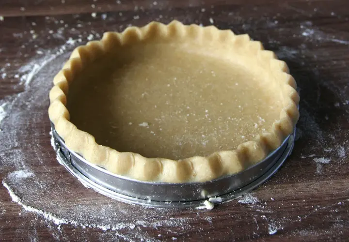 Une pâte brisée maison, prête à être garnie, repose dans un moule à tarte sur une planche en bois.