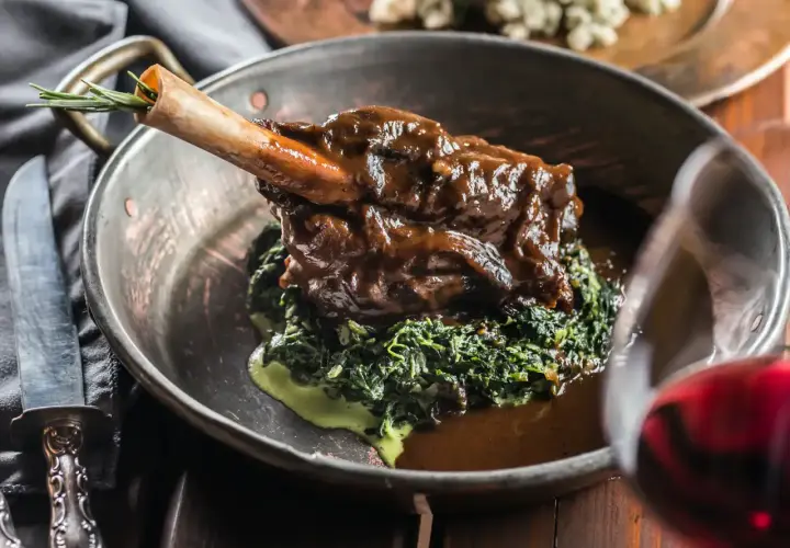 Un gigot de 7 heures, tendre et savoureux, servi sur un lit d'épinards crémeux dans un plat en cuivre. Une touche de romarin sur l'os promet un délice.