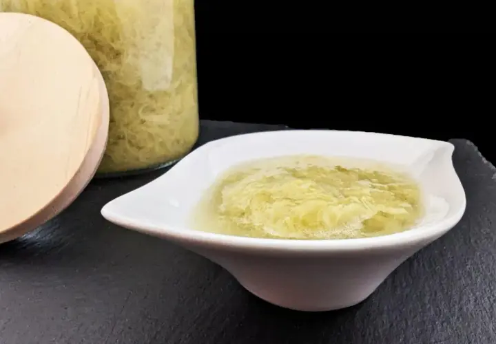 Compote de rhubarbe maison dans un bol blanc, à côté d'un bocal en verre rempli de cette délicieuse préparation.