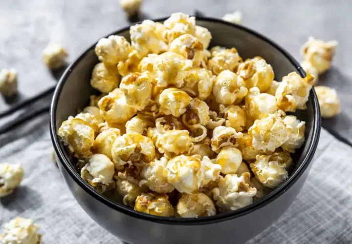 Un bol rempli de pop corn sucré, avec quelques grains éparpillés autour. Parfait pour une soirée cinéma !