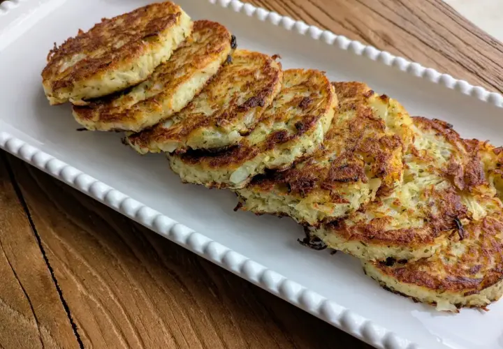 Six galettes de pomme de terre dorées et croustillantes, disposées sur un plat blanc festonné, prêtes à être dégustées.