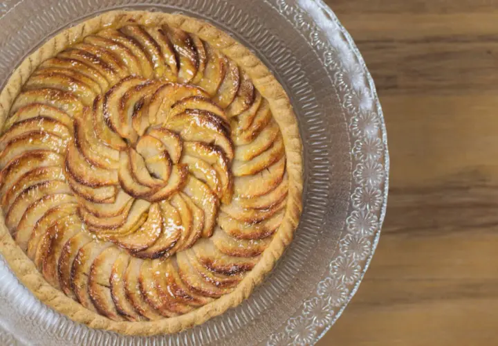Tarte aux pommes magnifiquement arrangée en spirale sur un plat en verre, prête à être dégustée.