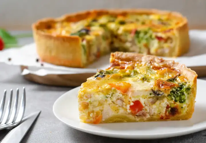 Une part de quiche savoureuse, garnie de poulet, brocolis et poivrons, repose sur une assiette. La pâte à quiche dorée est parfaite.