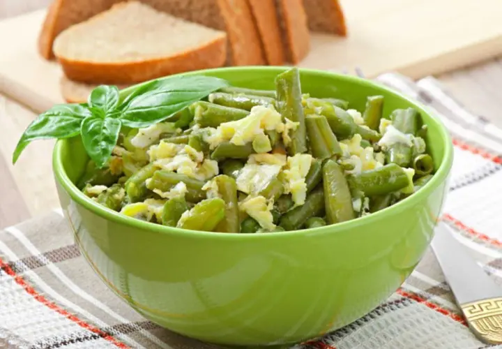 Salade haricots verts fraîchement préparée, garnie de basilic, servie dans un bol vert vif.