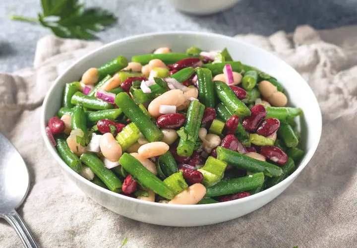Salade colorée de haricots verts, haricots blancs et haricots rouges, avec des oignons rouges et du céleri. Un plat frais et savoureux.