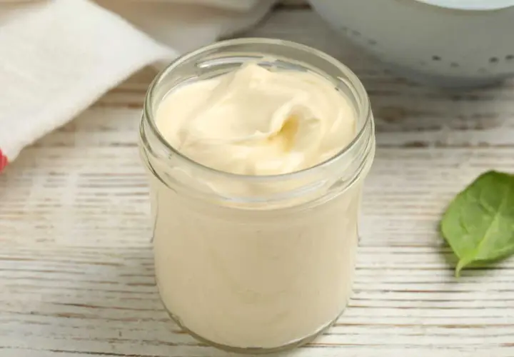 Un pot en verre rempli d'une onctueuse mayonnaise sans huile, sur une table en bois. Une feuille verte à côté.