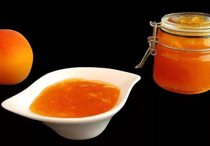 Un abricot frais à côté d'une coupelle de confiture abricot peu sucrée et d'un bocal de cette même confiture.