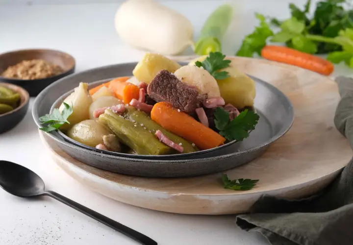 Pot-au-feu Cookeo avec viande, légumes (carottes, poireaux, oignons) et lardons, servi dans une assiette grise.