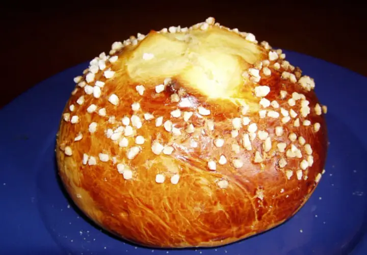 Mouna dorée parsemée de sucre perlé sur une assiette bleue.