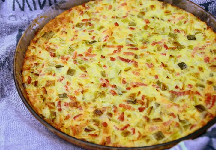 Une quiche aux légumes dorée et appétissante, garnie de poireaux et de lardons, sortant du four dans un plat en verre.