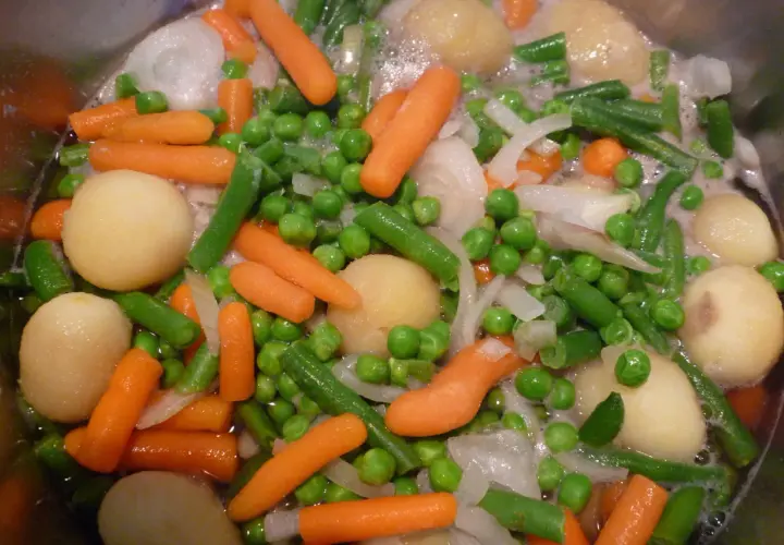 Gros plan sur une jardinière de légumes bouillant : carottes, petits pois, haricots verts, pommes de terre et oignons.
