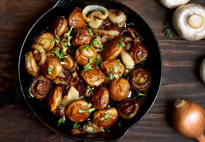 Champignons de Paris sautés à l'ail et aux oignons dans une poêle en fonte, parfaits pour une recette simple et savoureuse.