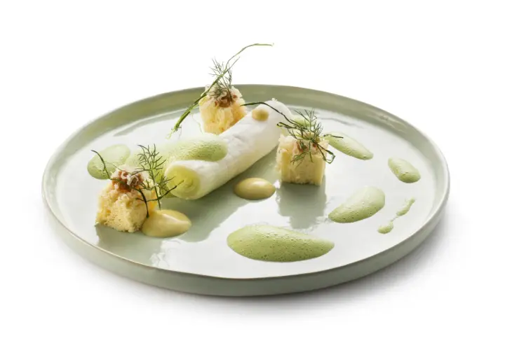 Poireaux à la crème, présentés avec des cubes de pain brioché, une sauce crémeuse et une mousse verte aérienne, le tout garni d'aneth.