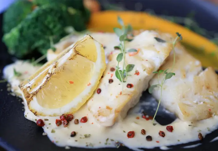 Filets de poisson nappés d'une sauce onctueuse, accompagnés d'une tranche de citron grillée et de légumes verts. Une sauce pour poisson parfaite pour sublimer ce plat.