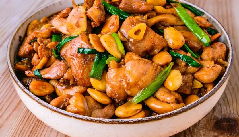 Un plat appétissant de poulet noix de cajou, garni d'oignons verts et d'ail, dans un bol sur une table en bois.