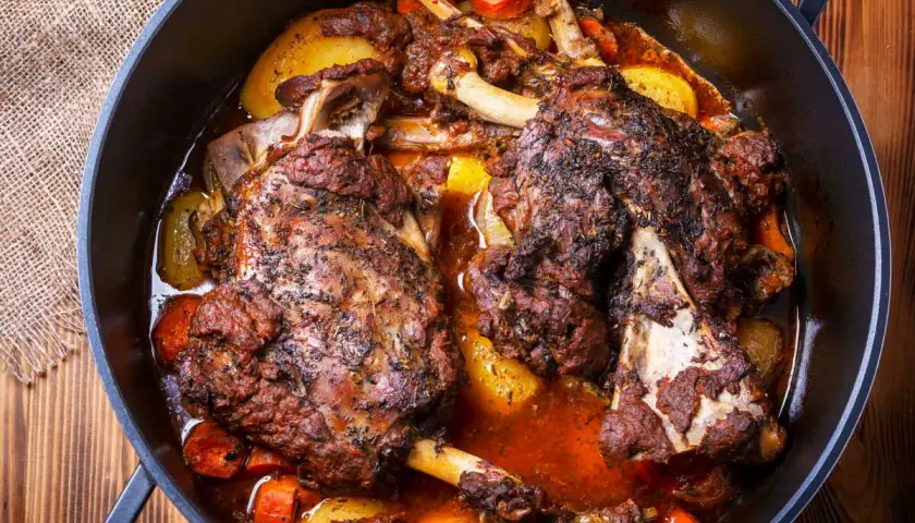 Deux épaules d'agneau en cocotte, tendres et savoureuses, mijotent avec des pommes de terre et des carottes dans un jus parfumé.
