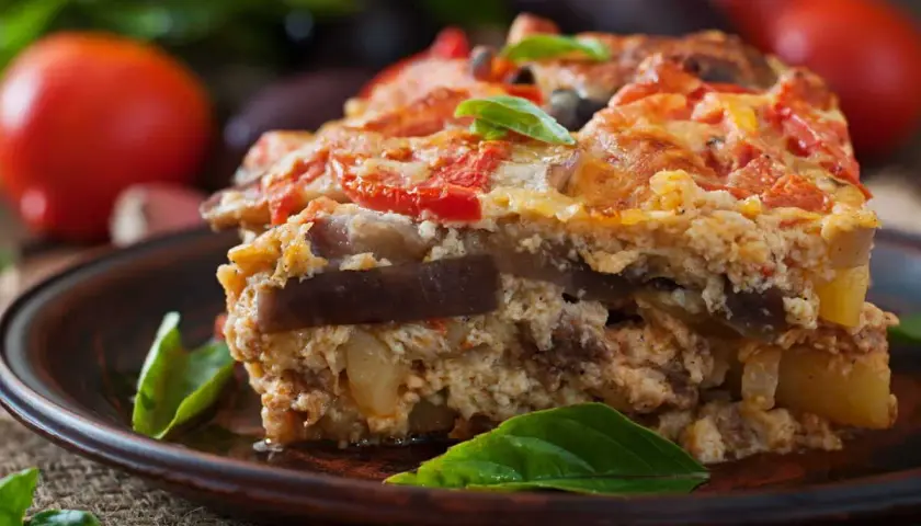 Un généreux flan de légumes, aux couches d'aubergines et de tomates, garni de basilic frais, sur une assiette en terre cuite.