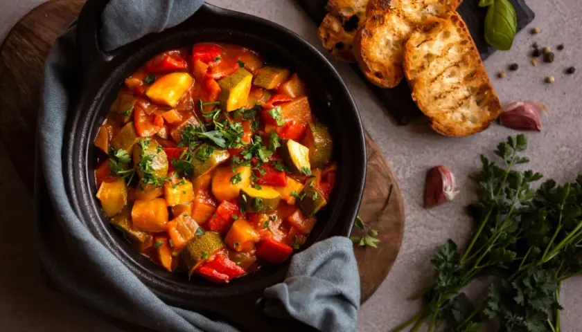 Ratatouille colorée dans un plat noir, servie avec des toasts grillés. Parfait pour savoir que manger avec une ratatouille.