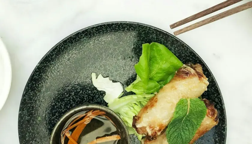 Deux nems dorés sur un lit de salade, accompagnés d'une coupelle de sauce nem maison et de baguettes.