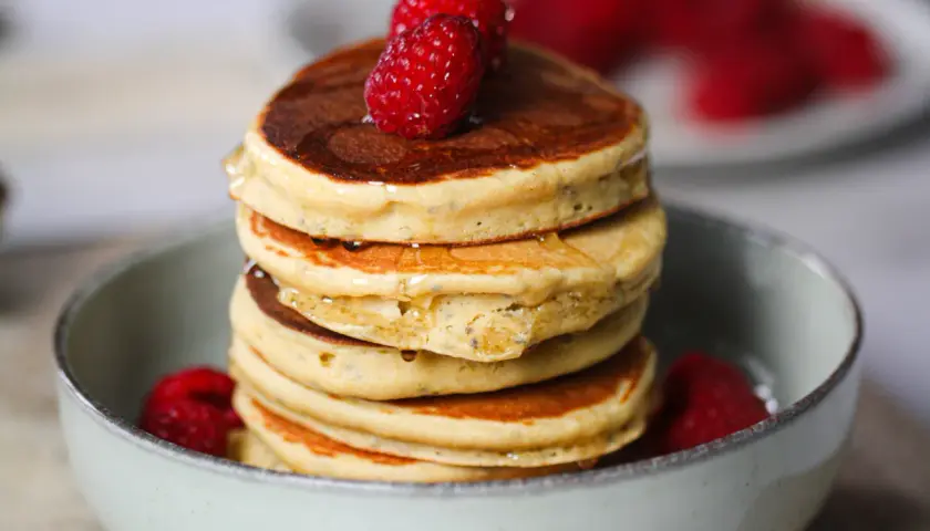 Pile de délicieux pancake sans gluten, garnis de framboises fraîches et nappés de sirop.