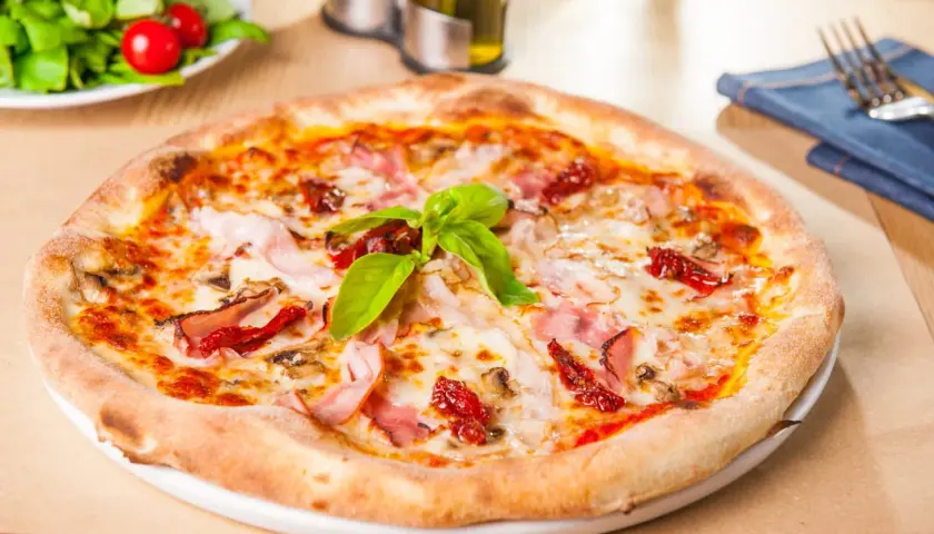 Une délicieuse pâte à pizza garnie de jambon, de tomates séchées et de basilic frais, prête à être dégustée.