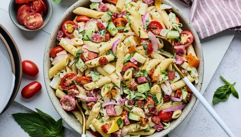 Salade de pâtes généreuse avec penne, tomates cerises, concombre, salami et oignons rouges. Un plat frais et coloré.