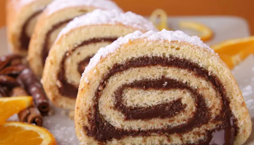 Tranches de roulé au chocolat saupoudrées de sucre glace, accompagnées d'oranges et de bâtons de cannelle.
