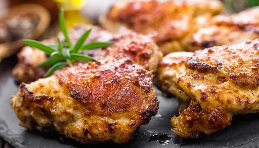 Délicieuses cuisses de poulet Cookeo dorées et croustillantes, garnies de romarin frais sur une assiette en ardoise.