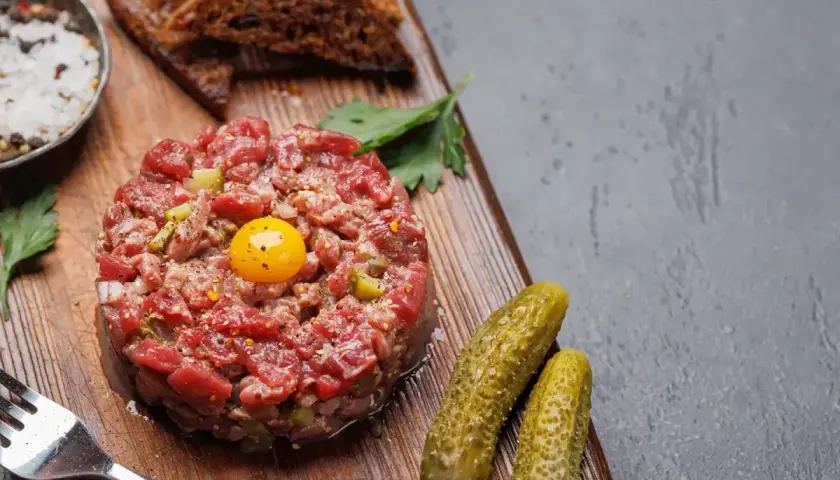 Un délicieux tartare de boeuf, garni d'un jaune d'œuf, servi avec des cornichons, du pain grillé et des épices.