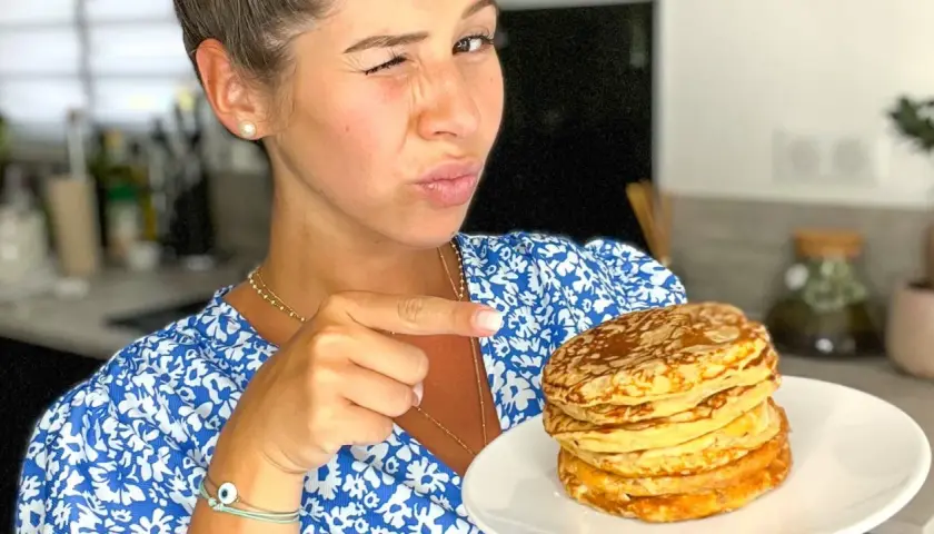 Une femme fait un clin d'œil et pointe du doigt une pile de pancakes banane sans oeuf sur une assiette.