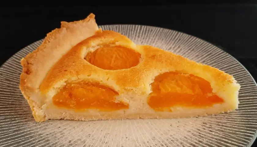 Tranche de tarte aux abricots classique, avec sa pâte dorée et ses fruits juteux, prête à être dégustée.