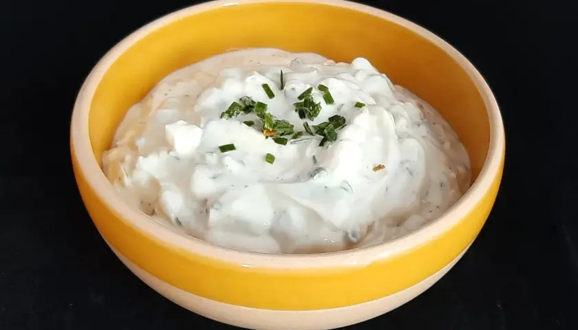 Sauce onctueuse à base de fromage blanc et de ciboulette fraîche, garnie de brins d'herbe verte.