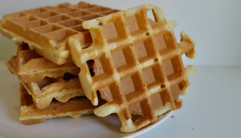 Pile de gaufres dorées sur une assiette blanche. La pâte à gaufre a été cuite à la perfection, offrant une texture croustillante et moelleuse.