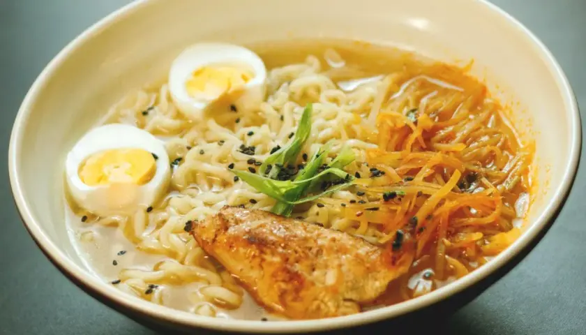 Un bol de recette ramen poulet, garni d'œufs durs, de poulet grillé, de nouilles et de ciboule.