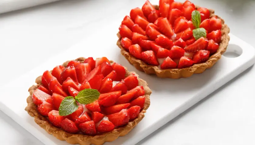 Deux tartelettes gourmandes aux fraises fraîches et crème pâtissière, ornées d'une feuille de menthe. Un délice estival.
