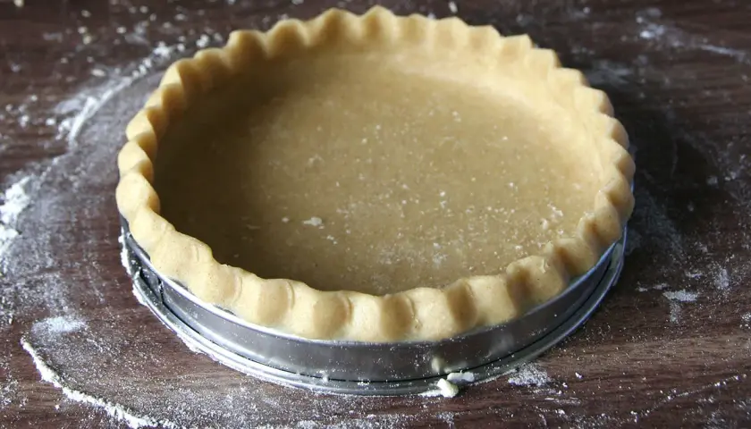 Une pâte brisée maison, prête à être garnie, repose dans un moule à tarte sur une planche en bois.