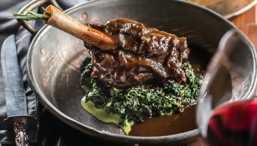 Un gigot de 7 heures, tendre et savoureux, servi sur un lit d'épinards crémeux dans un plat en cuivre. Une touche de romarin sur l'os promet un délice.