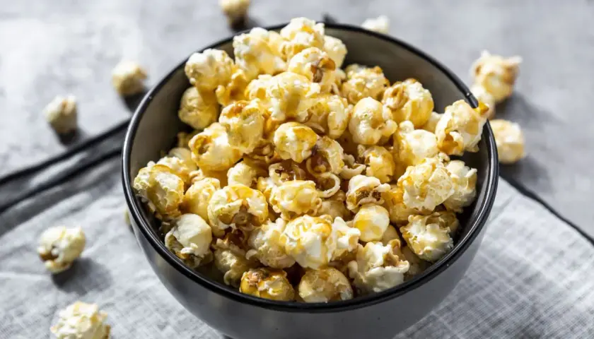 Un bol rempli de pop corn sucré, avec quelques grains éparpillés autour. Parfait pour une soirée cinéma !