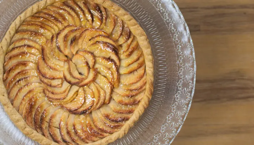 Tarte aux pommes magnifiquement arrangée en spirale sur un plat en verre, prête à être dégustée.
