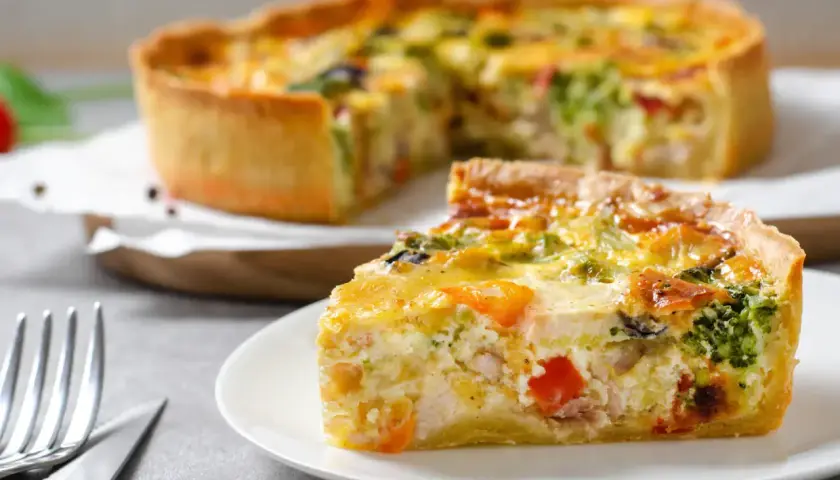 Une part de quiche savoureuse, garnie de poulet, brocolis et poivrons, repose sur une assiette. La pâte à quiche dorée est parfaite.